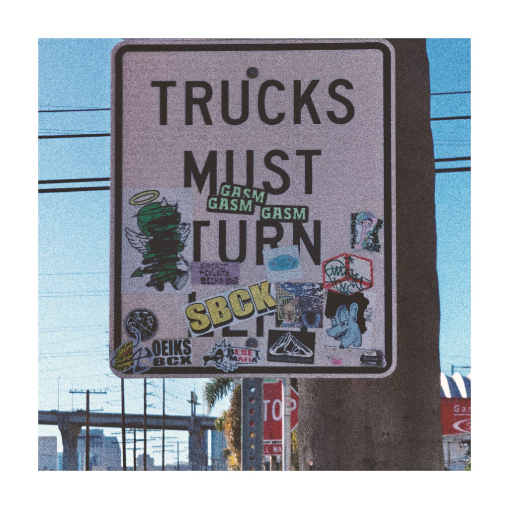 A street sign that reads TRUCKS MUST TURN. Three stickers with the name GASM are below the word MUST, making the sign read TRUCKS MUST GASM GASM GASM.