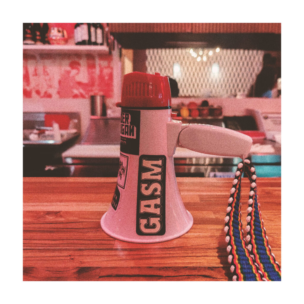 A small megaphone sitting on a wooden counter has a sticker with the name GASM.